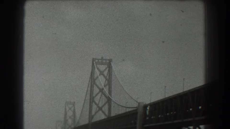 1939 San Francisco home-movie view of a suspension bridge tower, cables, and deck structure against a hazy sky.