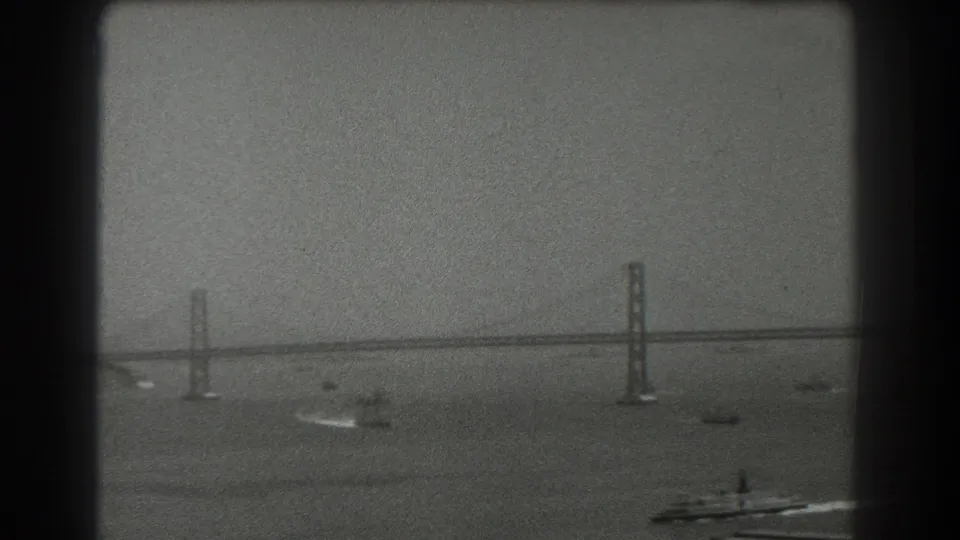 A distant 1939 San Francisco Bay view shows bridge towers and span above open water, with several small boats leaving pale wakes.