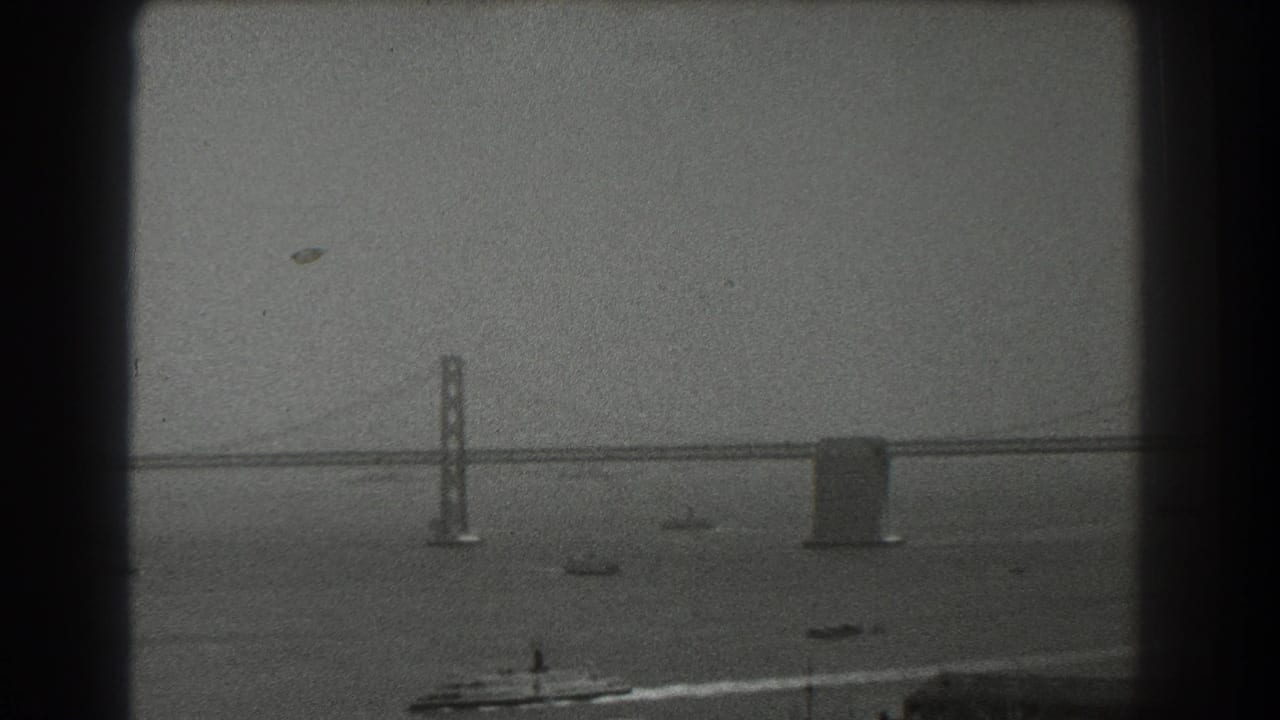 Bay Bridge over San Francisco Bay with small boats under a hazy sky.