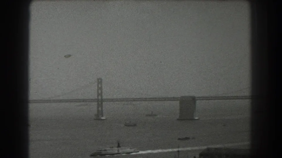 1939 San Francisco Bay view showing the Bay Bridge span, piers, and several small boats on hazy water.