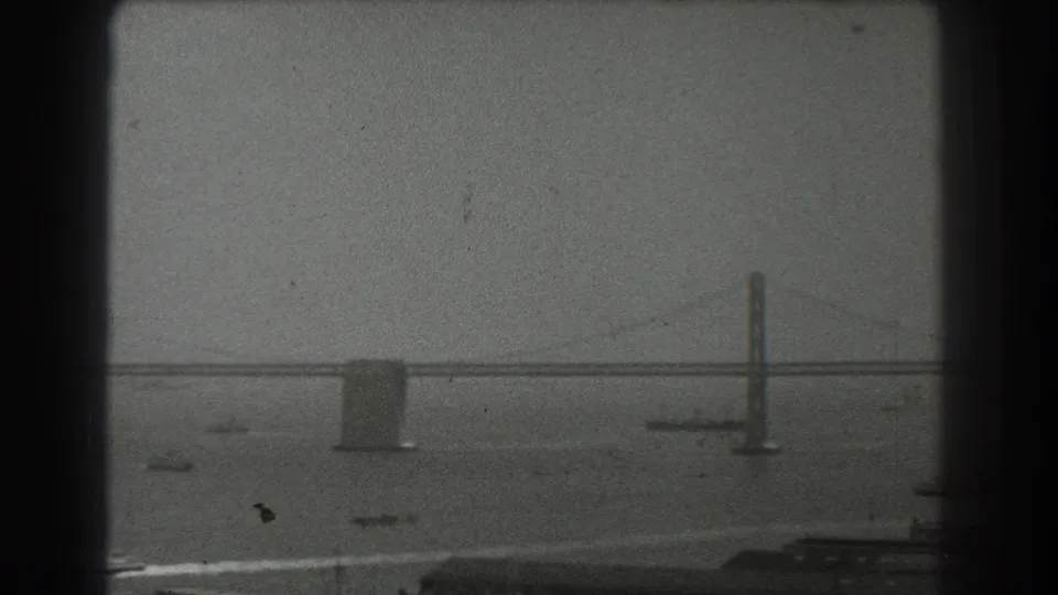 San Francisco Bay Bridge seen through soft haze, with small boats scattered beneath the span in a 1939 8mm frame.
