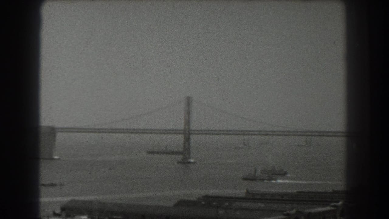 Hazy suspension bridge over a bay with boats and waterfront structures below.