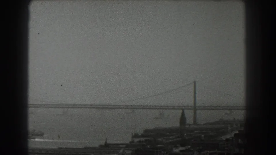 Late-1930s San Francisco bay footage showing a suspension bridge span, tower, water traffic traces, and industrial shoreline foreground.