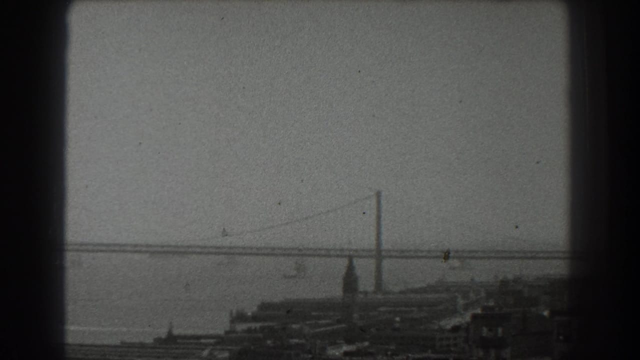 Distant suspension bridge over San Francisco Bay with waterfront buildings below.