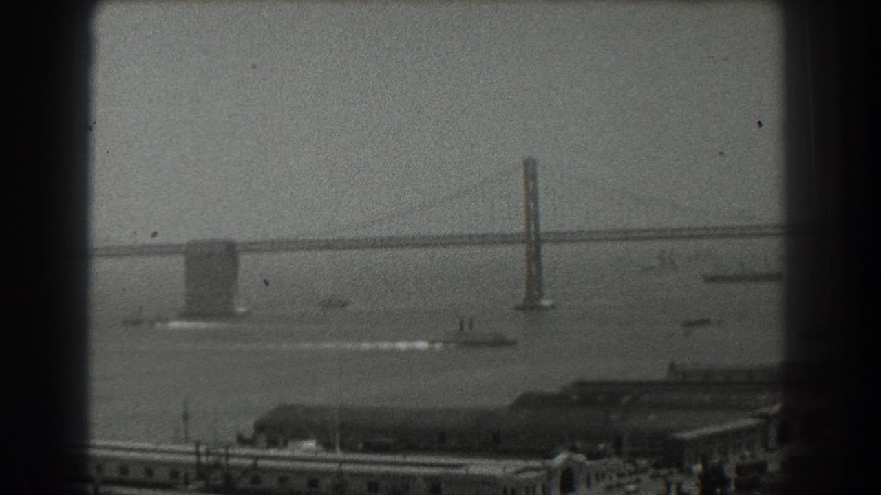 1939 8mm view of San Francisco Bay with a suspension bridge, small boats, pier buildings, and dark film gate borders.