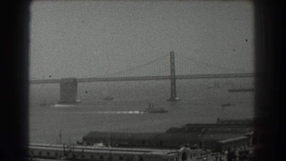 1939 8mm view of San Francisco Bay with a suspension bridge, small boats, pier buildings, and dark film gate borders.