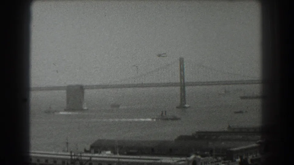 San Francisco Bay in 1939, showing a bridge tower, ferry wake, scattered boats, and low waterfront buildings on 8mm film.
