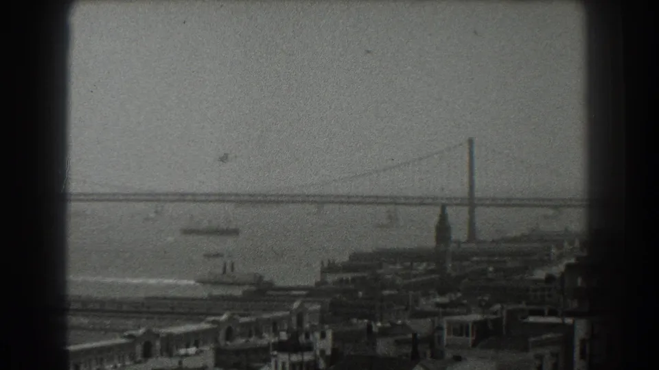 Elevated 1939 San Francisco waterfront view with pier buildings, bay vessels, and a distant suspension bridge across the water.