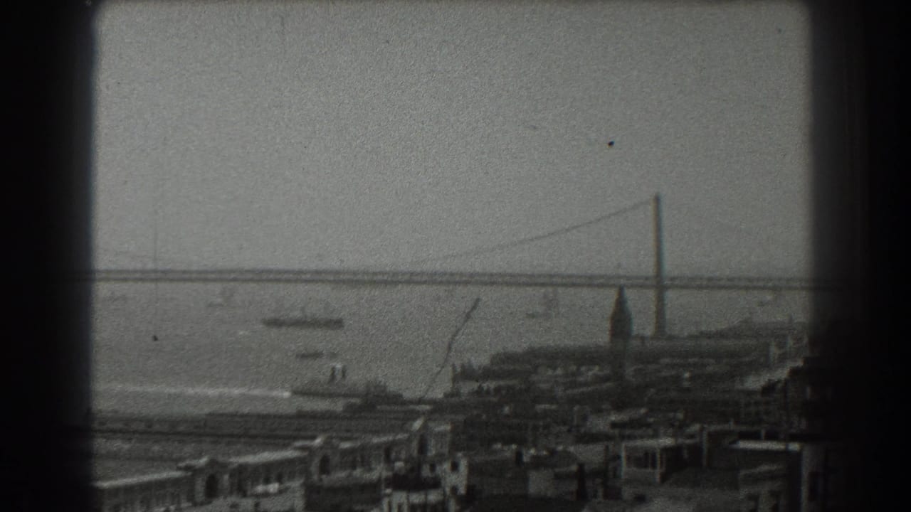 1939 San Francisco home-movie frame showing the Bay Bridge across the water, boats in the bay, and waterfront buildings below.