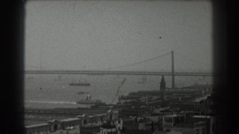 1939 San Francisco home-movie frame showing the Bay Bridge across the water, boats in the bay, and waterfront buildings below.