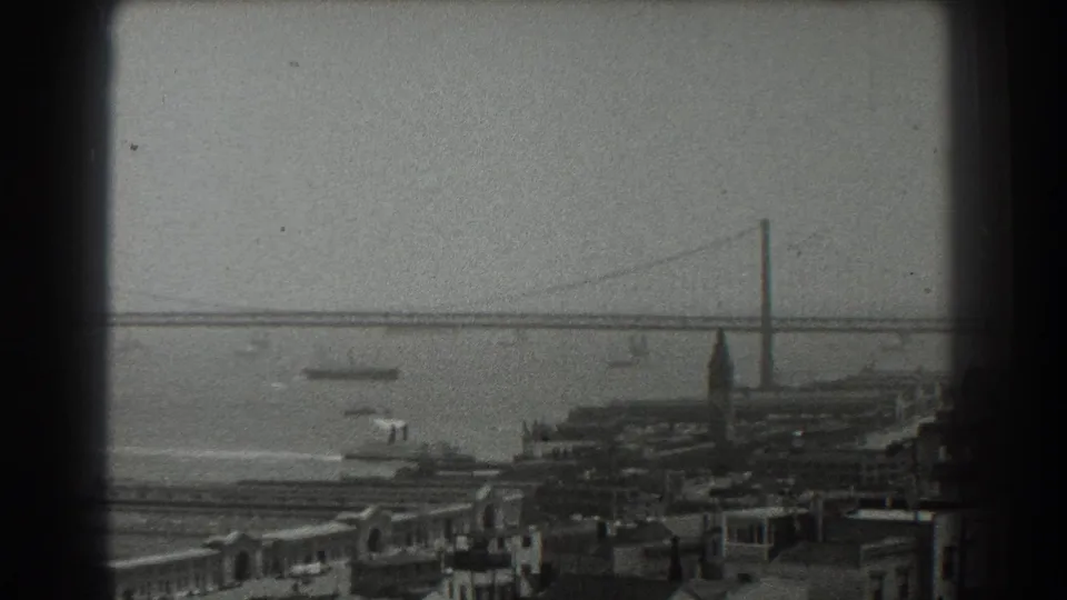 1939 San Francisco frame with the Bay Bridge spanning the background and small boats near the waterfront in soft 8mm focus.