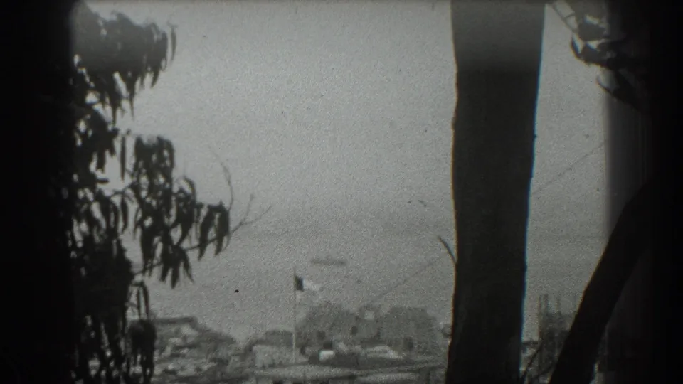 1939 San Francisco home-movie view over the bay with foreground trees, a flag, waterfront buildings, and faint bridge detail beyond.