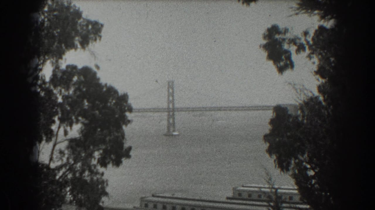 1939 San Francisco home-movie frame showing the Golden Gate Bridge far across the bay through foreground trees.