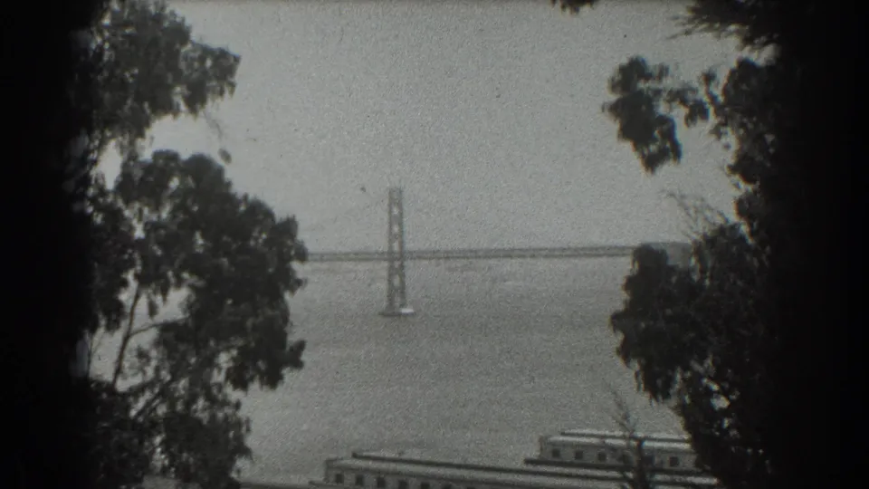 1939 San Francisco home-movie frame showing the Golden Gate Bridge far across the bay through foreground trees.