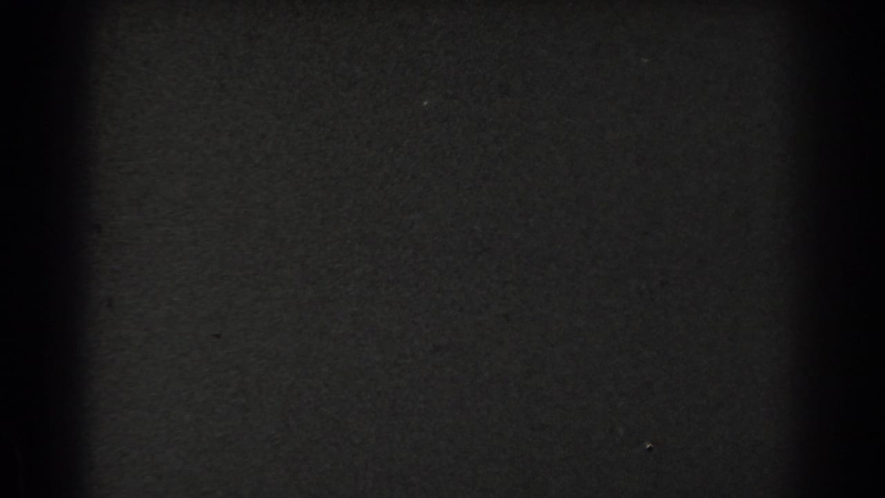 A mostly obscured black-and-white 8mm frame from the San Francisco clip, with part of a staircase and a suited figure barely visible at the right.