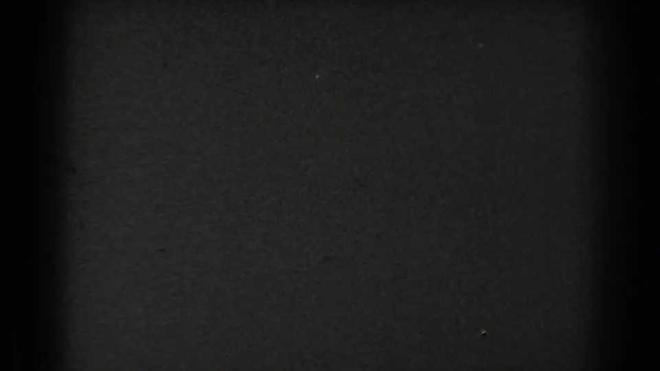A mostly obscured black-and-white 8mm frame from the San Francisco clip, with part of a staircase and a suited figure barely visible at the right.