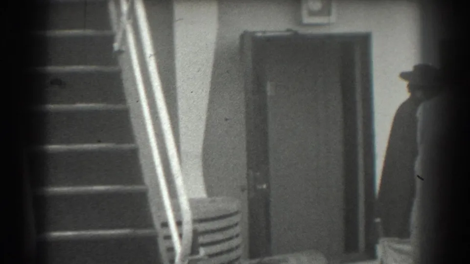 The man appears in profile or silhouette as he walks past a closed doorway and stair rail in 1939 San Francisco footage.