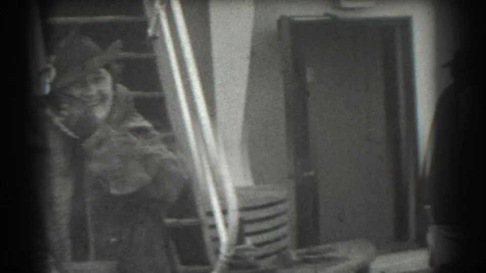 1939 San Francisco frame of a woman in period coat and hat smiling while moving near the ship gangway.