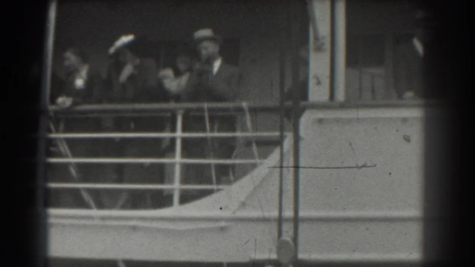 1939 San Francisco home-movie frame showing passengers in hats and suits behind railings on a ship deck.