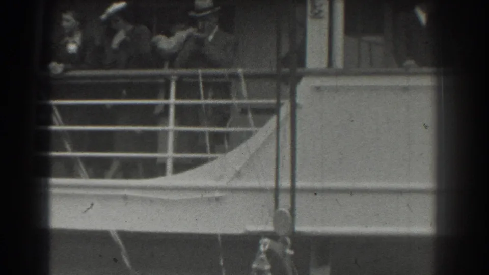 Black-and-white 8mm frame of passengers on a ship deck, with late-1930s clothing and railings visible.