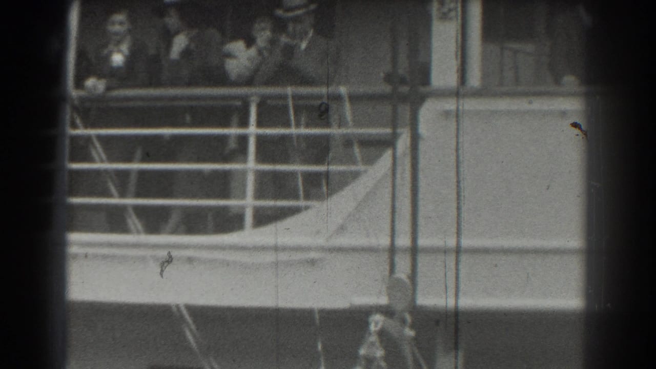 Passengers stand behind a ship railing, with several figures in hats and dark clothing visible.