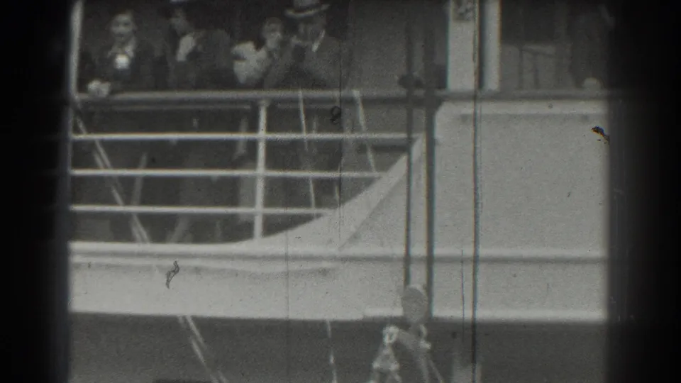 In supported 1939 San Francisco 8mm footage, passengers stand and talk behind a metal railing on a cruise ship deck.