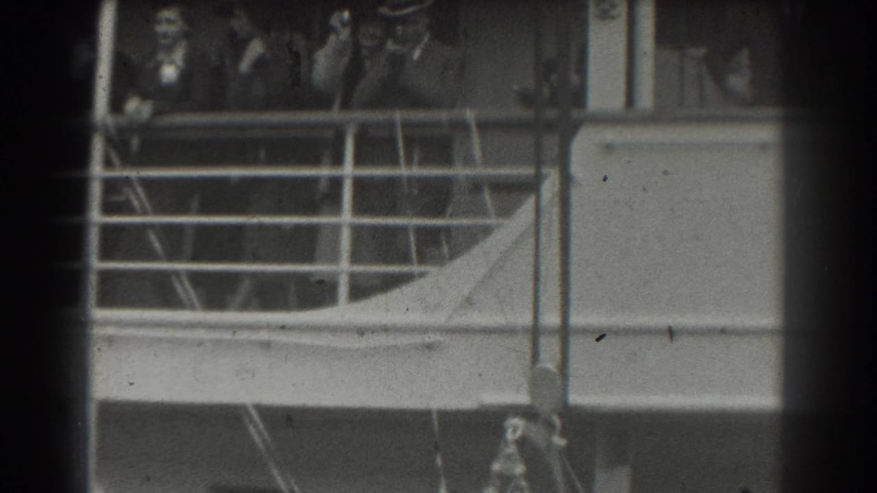 A group of passengers stands near a railing on a ship deck, partly obscured by film-frame borders.