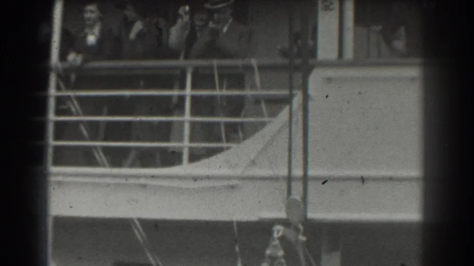Passengers in period clothing appear behind a ship railing in 1939 San Francisco home-movie footage, with faces faintly visible.