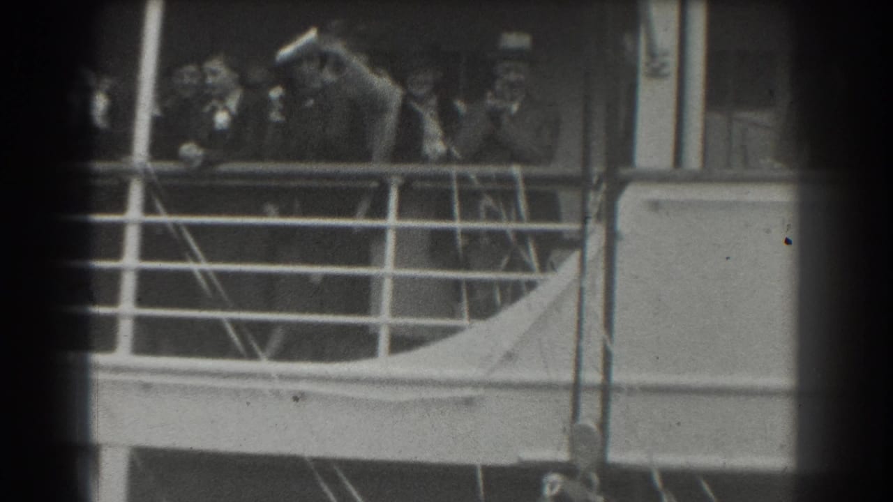 Adults in formal clothing stand behind a ship railing, with one person leaning forward near the left side.