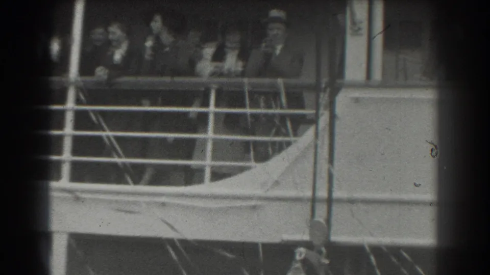 Well-dressed adults on a ship deck in the 1939 San Francisco clip look outward from behind a metal railing.