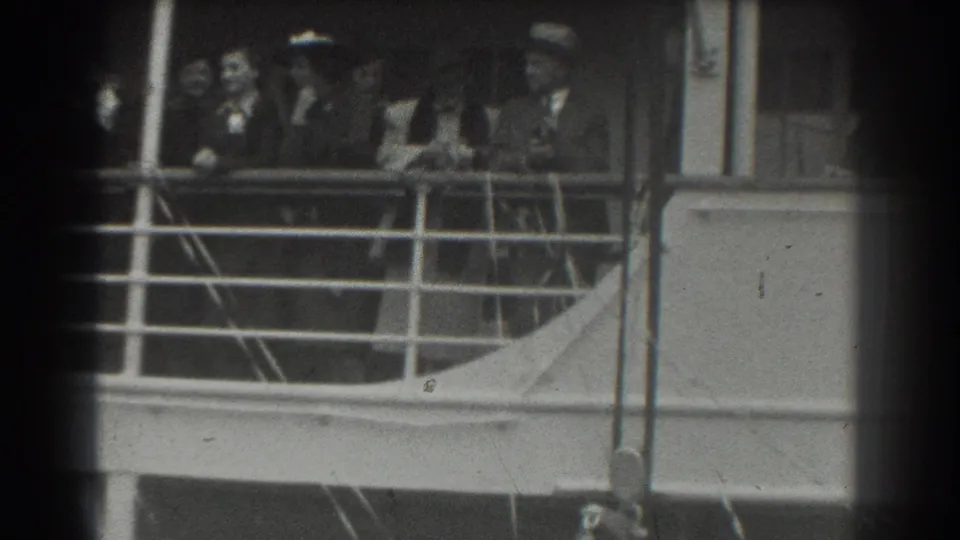 Near the end of the 1939 San Francisco ship-deck clip, adults in formal clothing continue looking and waving from behind the railing.