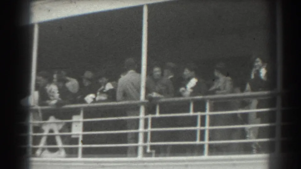 Black-and-white 8mm frame of ship passengers on deck, likely in San Francisco based on clip metadata, with formal period clothing visible.