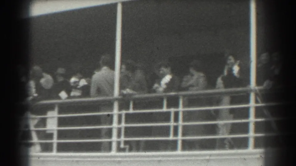 Passengers remain along the ship deck railing in a 1939 home-movie view, softened by grain and partial frame obstruction.