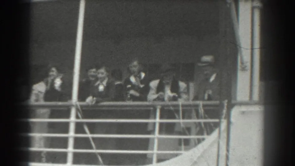 Passengers in late-1930s attire appear along a ship deck railing in black-and-white home-movie footage.