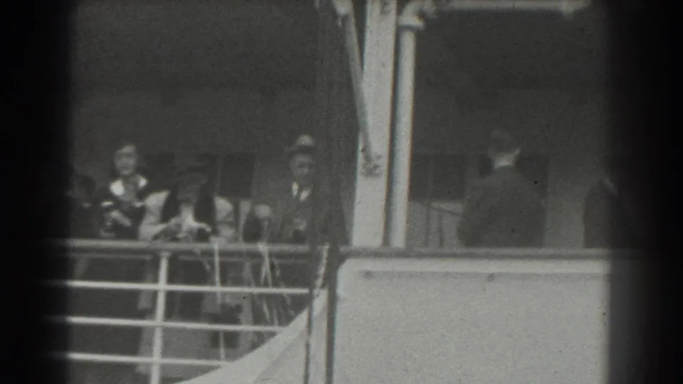 A 1939 home-movie frame shows passengers on a ship deck, including a figure turned away near the cabin side.