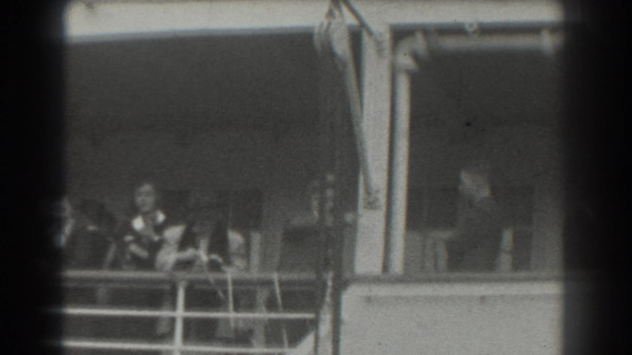 Well-dressed passengers stand behind a ship deck railing in a shaded area.