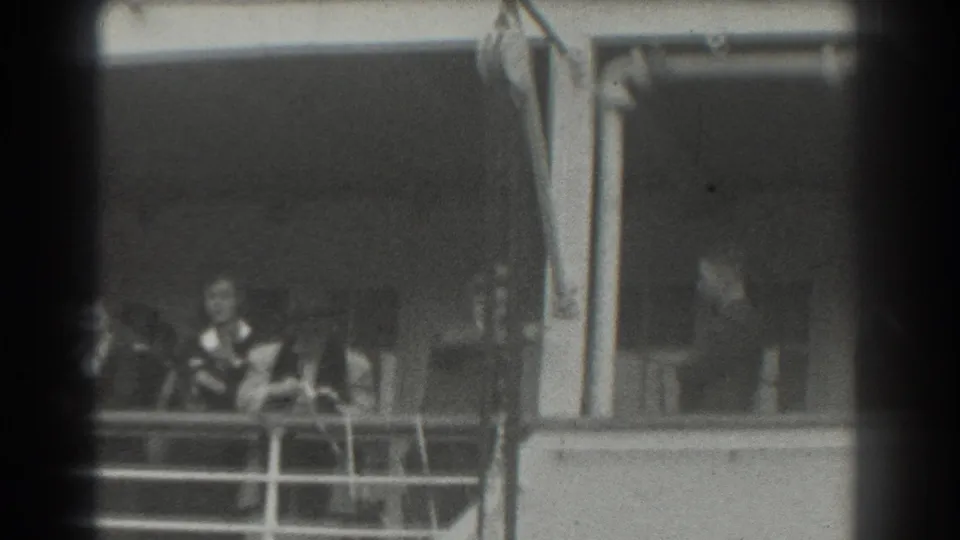 In 1939 San Francisco footage, suited passengers and women in formal clothing stand behind a metal railing on a ship deck.