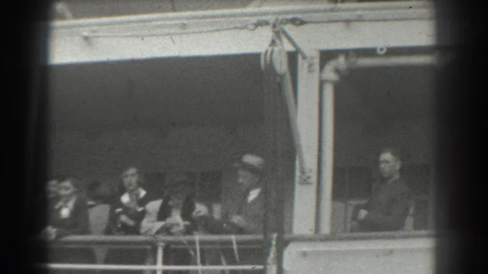 A 1939 San Francisco home-movie frame shows passengers in suits, hats, and dresses gathered along a ship deck railing.