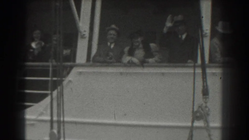 In 1939 San Francisco home-movie footage, passengers in hats and dress clothing stand on a ship deck and wave from behind the railing.