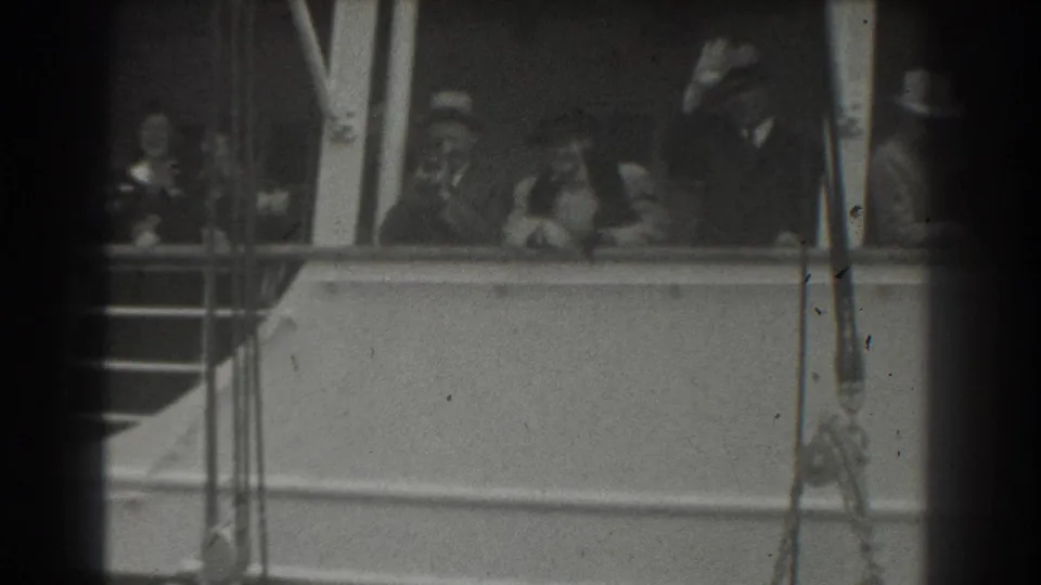 Passengers on a San Francisco ship deck wave from behind the railing, including a man at right raising his hat or hand.