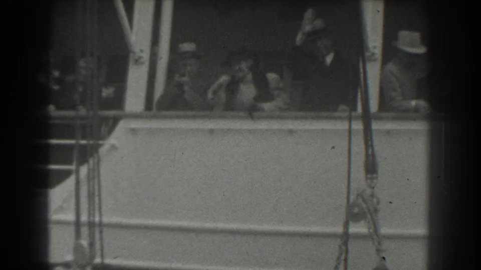 The 1939 home-movie frame shows passengers in period clothing standing at the rail of a ship in San Francisco, waving toward unseen people.