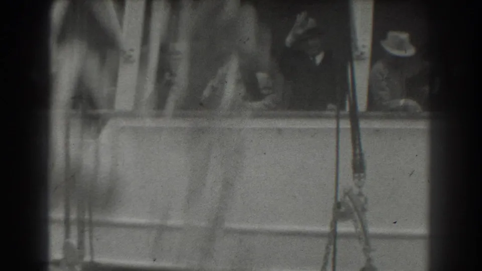 A blurred foreground movement crosses the frame as passengers on the ship deck remain near the railing during the farewell scene.