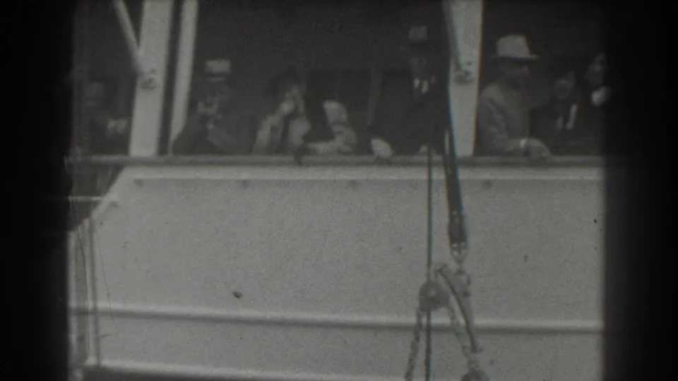 1939 San Francisco ship-deck frame with passengers looking out from the rail and a man in a light hat at the side.