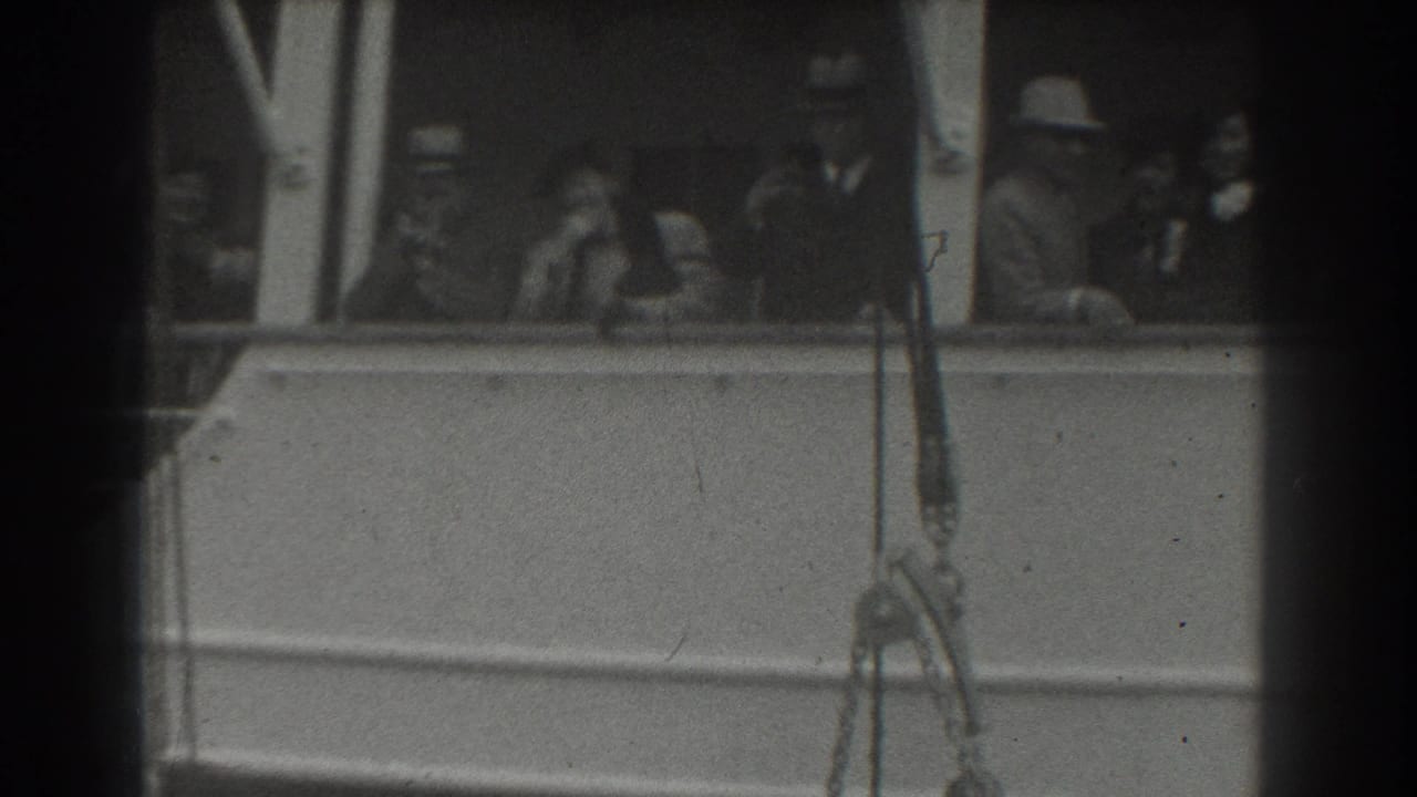 Passengers stand behind a ship railing, with dark film borders and rigging in the foreground.