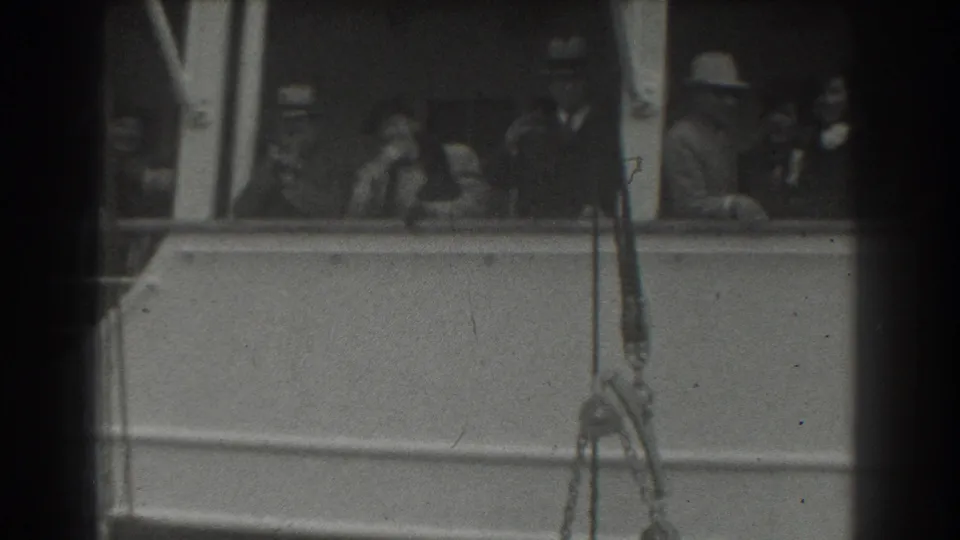 In 1939 San Francisco footage, adults in hats and coats stand along a ship deck railing during a departure.