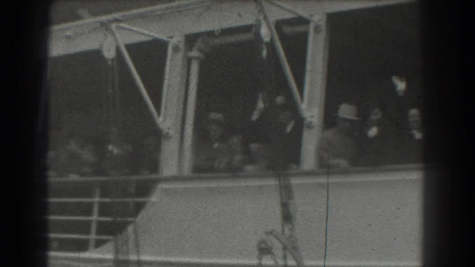 Adults aboard a departing ship in San Francisco wave from the deck beside railings and painted supports.