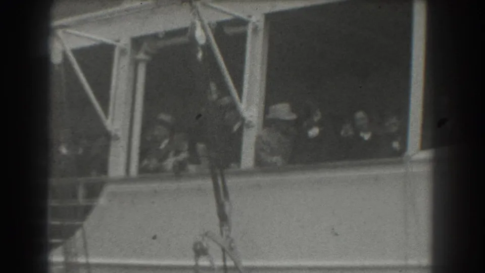 Passengers aboard a ship in San Francisco appear through cabin windows, some facing outward toward the camera.