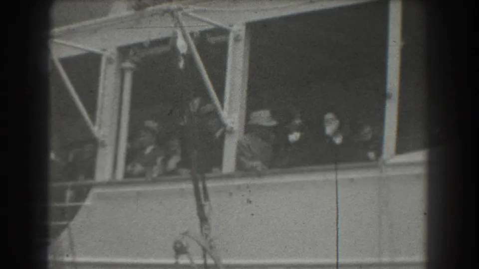 Black-and-white 8mm frame of passengers clustered behind ship windows during a 1939 San Francisco sailing scene.