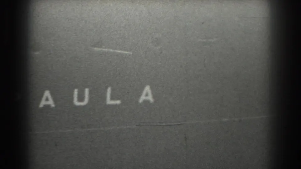 Black-and-white 8mm frame showing a partial title-card or leader fragment with the letters A U L A visible.