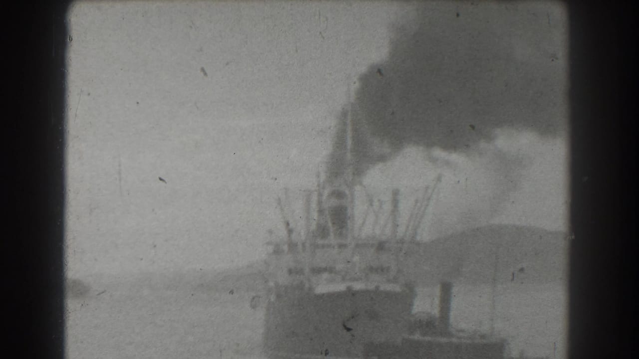 A distant vessel in San Francisco harbor appears beneath a heavy smoke plume, with shoreline shapes faintly visible through aged 8mm film texture.